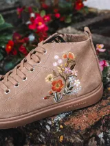 Botín de cuero serraje color beige, con cordones y detalle de flores bordadas en el lateral. Cuenta con suela plana de goma y cierre de cremallera lateral.