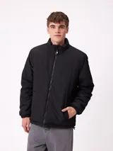 Campera reversible de nylon con cuello alto y cierre frontal. Un lado es de color gris liso con logo bordado, mientras que el otro lado presenta un estampado abstracto en tonos azules. Cuenta con bolsillos laterales y puños elásticos.