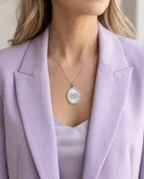 Dije ovalado de plata 925 con base de nácar, borde decorado con circonias y diseño central de nene y nena.