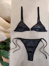 Conjunto de bikini negro con acabado efecto cuero, compuesto por un corpiño triangular con cierre frontal metálico y bombacha tipo vedetina con tiras laterales ajustables.