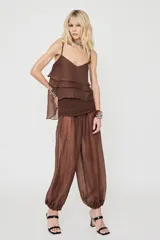 Pantalón marrón de corte ancho y estilo balloon, confeccionado en tejido translúcido con textura sutil y puños fruncidos en los tobillos.