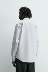 Camisa blanca de corte slim fit, confeccionada en tejido de algodón. Presenta cuello italiano, manga larga con puño abotonado y cierre frontal de botonadura.