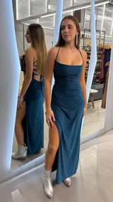Vestido largo de fiesta color verde oscuro con brillo sutil, corte al cuerpo con fruncidos en el torso, escote recto, tirantes finos cruzados en la espalda y tajo profundo en la pierna.