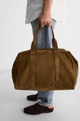 Bolso de mano marrón de cuero con acabado serraje. Tiene un compartimento principal con cierre de cremallera, dos bolsillos interiores (uno con cremallera) y asas de mano de cuero.