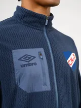 Buzo de micropolar azul con medio cierre frontal, cuello alto y bolsillo con cierre en el pecho. Presenta el logo de Umbro y el escudo del Club Nacional de Football.