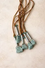 Collar con tiras de cuero y dije de piedra en bruto con detalles metálicos y cuentas verdes.
