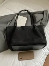 Bolso tipo tote de diseño minimalista en color negro, con textura suave y doble asa larga para llevar al hombro.
