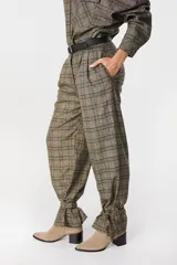 Pantalón de tiro medio con estampado a cuadros, corte holgado y pinzas en la cintura. Presenta un diseño distintivo con tiras ajustables en los tobillos que permiten crear un efecto fruncido.