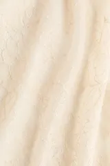 Pañuelo de cadera corto confeccionado en encaje de color beige, con tiras finas para atar en un lateral y terminaciones en ondas.