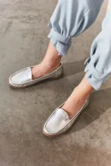 Mocasines de cuero color dorado con acabado texturizado, diseño clásico de punta redondeada y costuras visibles en el empeine. Cuentan con suela plana y flexible.