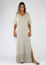Vestido largo de punto con hilo metalizado, color beige, escote en V, mangas cortas y detalle de flecos en el ruedo.