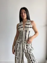 Top de cuello halter con escote en V profundo, confeccionado en tela slab con estampado de rayas abstractas negras sobre fondo beige. Se ajusta mediante lazos en el cuello y la espalda, con terminación en punta en la parte frontal.