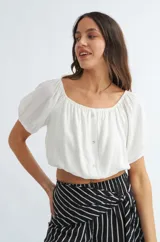 Blusa blanca de poliéster, corte crop top, con escote off shoulder, mangas cortas abullonadas y cierre frontal con botones.