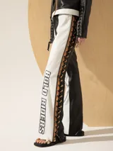 Pantalón de cuero blanco y negro, de corte recto, con detalles de cuero color camel. En los laterales, lleva una pieza de cuero con cordones de cuero negro y camel trenzados. En el delantero lleva bordados de hilo y cuero plata.
