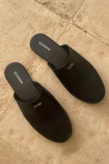 Slippers de cuero negro con logo metálico en el lateral.