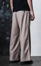 Pantalón sastrero de corte oversize en color beige, con pinzas frontales profundas que aportan volumen y movimiento. Presenta cintura ancha, bolsillos laterales y bolsillos tipo ojal en la parte trasera, con detalle de botones en el ruedo.