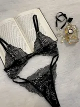 Conjunto de lencería compuesto por bralette triangular y tanga, confeccionado en encaje bitono negro y blanco. El bralette presenta cierre frontal con broche de gancho y breteles regulables. La tanga es de estilo colaless con laterales regulables mediante herrajes metálicos.