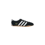 Championes Adidas Tokyo Core Black confeccionados en gamuza negra, con las tres franjas características en blanco y suela de goma marrón. Incluye la inscripción "Tokyo" en letras doradas al costado.