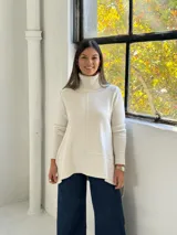 Sweater de punto color beige con cuello alto tipo polera, diseño holgado y costuras visibles en el frente.
