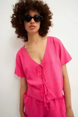 Camisa fucsia de manga corta con escote en V y cierre frontal mediante múltiples lazos anudados.