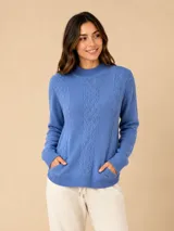 Buzo de punto color azul, con cuello redondo, diseño de trenzas verticales en el frente y bolsillos laterales. Presenta puños y ruedo acanalados.