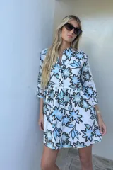 Vestido corto de silueta relajada con estampado floral en tonos celestes y azules sobre fondo blanco. Presenta cuello mao, cierre frontal con botones, mangas tres cuartos y corte con volados en la falda.