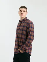 Camisa de franela a cuadros con cuello button-down, manga larga y botones de madera. Presenta dos bolsillos tipo parche en el frente con cierre de botón.