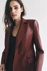 Blazer de cuero sintético en color beige, con cuello solapa, manga larga y bolsillos con solapa en el frente. Cierre frontal cruzado con botones a tono.