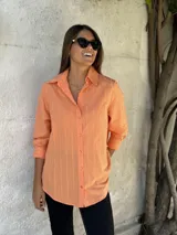 Camisa color salmón con cuello clásico, cierre frontal con botones y mangas largas con puños abotonados.