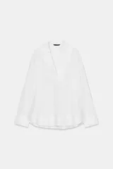 Blusa blanca confeccionada en lino, con cuello polo, escote en V y mangas largas amplias. Presenta un diseño holgado y bajo asimétrico.