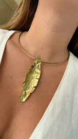 Gargantilla dorada rígida con dije colgante en forma de hoja texturada.