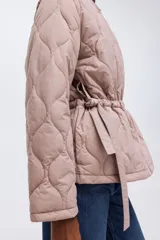 Campera acolchada de nylon guateado en color rosado, con cuello redondo, cierre frontal y cordón ajustable en la cintura con tiras colgantes. Presenta diseño acolchado con patrón de rombos, mangas largas y hombros caídos.