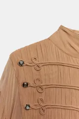 Vestido largo de viscosa en color tostado, con cuello subido y manga larga terminada en puño. Cuenta con cintura ajustable con lazadas, forro interior, bajo evasé y cierre frontal con alamares y botones.