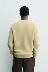 Sweater de punto canalé color beige, con cuello redondo y mangas largas con diseño raglán.