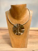 Gargantilla rígida plateada con dije circular texturizado.