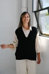 Chaleco de punto negro con escote en V profundo y diseño de trenzas verticales en el frente. Presenta un corte holgado y terminaciones en tejido acanalado.