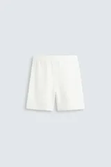 Bermuda de algodón color beige claro, de corte regular fit, con cintura elástica ajustable mediante cordón. Presenta bolsillos laterales y un bolsillo trasero de vivo.