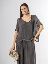 Vestido largo de seda italiana en color gris oscuro, con falda larga lisa, forro y cintura elastizada. Posee una sobrecapa con detalles de paillettes en los bordes de las mangas y la cintura.