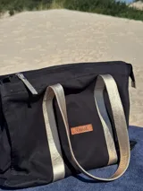 Bolso tipo tote bag negro con detalles dorados en las asas y en el logo.