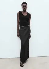 Falda larga de lino color negro, tiro medio, diseño estilo lápiz con abertura en la parte posterior y cierre de cremallera lateral.