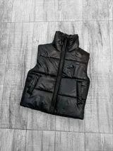 Chaleco puffer negro con cuello alto y cierre frontal con cremallera. Tiene bolsillos laterales y diseño acolchado.