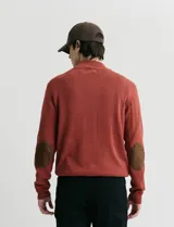 Sweater de punto color verde oliva, con cuello alto y medio cierre frontal. Presenta coderas en símil nappa y puños acanalados.