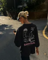 Remera oversize negra con diseño gráfico en la espalda que incluye la inscripción "Kaboa Radio" y un personaje ilustrado, de corte amplio y mangas cortas.