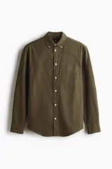 Camisa H&M de algodón Oxford verde militar con cuello americano, bolsillo frontal en el pecho, mangas largas con puños abotonados y botones blancos contrastantes.