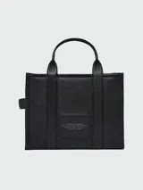 Cartera tipo tote de cuero granulado color tostado, con diseño estructurado y rectangular. Presenta doble asa superior fija y una correa larga ajustable y extraíble. En el frente, destaca el logo estampado con la inscripción 'THE TOTE BAG MARC JACOBS'.