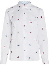 Camisa blanca de manga larga con cuello clásico y bolsillo frontal. Presenta un estampado repetitivo de pequeñas flores bordadas en tonos rojo, azul y negro. El interior del cuello tiene un detalle de rayas azules y blancas.