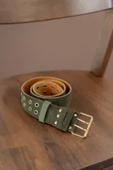 Cinturón de gamuza color verde oliva con doble hilera de ojalillos metálicos y hebilla cuadrada de metal envejecido.