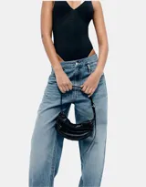 Bolso tipo hobo de cuero sintético negro, con efecto arrugado o fruncido en la parte superior y cierre de cremallera plateada. Posee una correa de hombro ajustable.