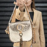 Morral de cuero vacuno color arena y peltre, con correa larga ajustable y removible, y correa corta de cadena y cuero. Tiene tapa superior con broche a presión y cierre superior. El interior está forrado en tela y contiene un bolsillo con cierre y otro más pequeño.