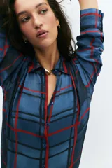 Camisa de manga larga con cuello solapa y cierre frontal con botones. Presenta un diseño de cuadros en tonos azules y rojos sobre un tejido semitransparente.